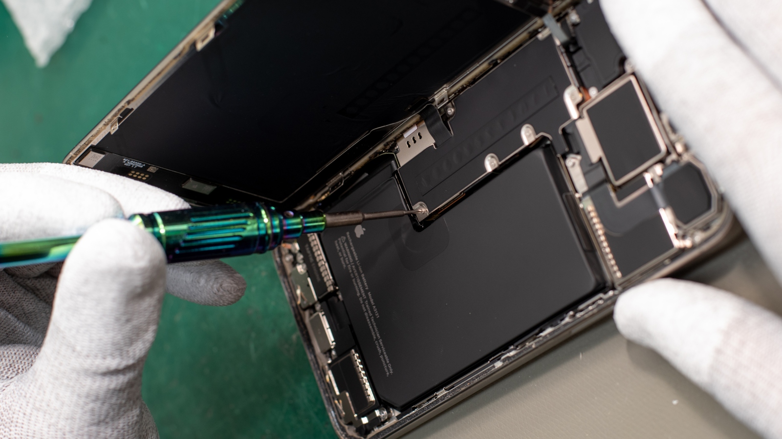 An opened smartphone showing its battery while hands lift the back cover.